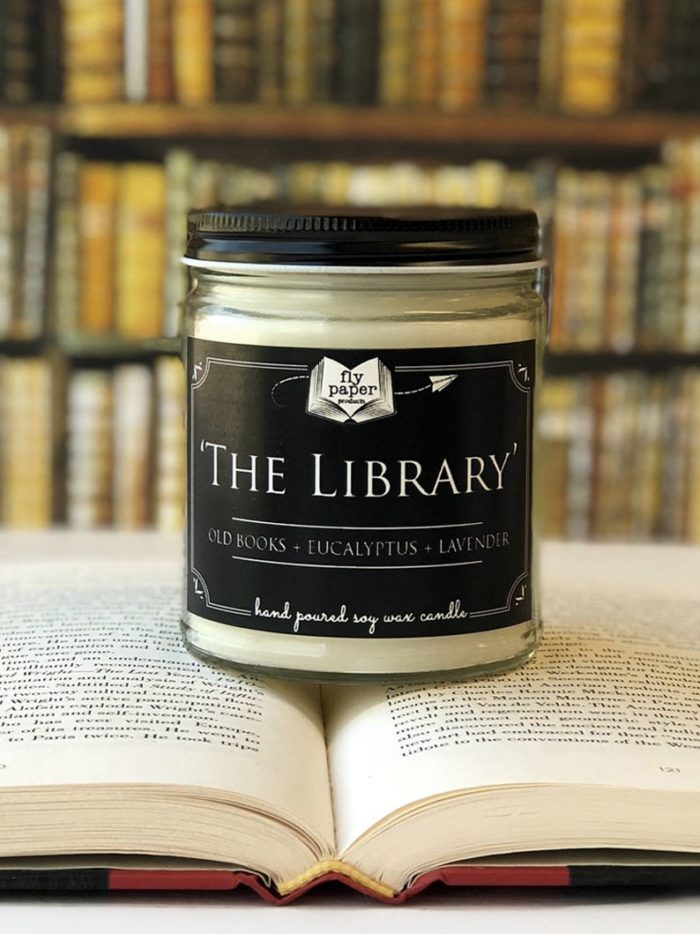 An off-white candle with a black label on an open book with blurred text